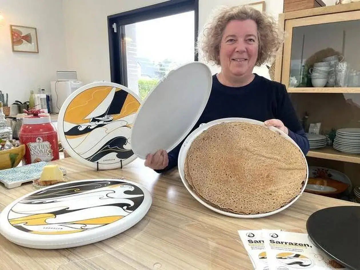 Une femme pr&eacute;sente une pile de cr&ecirc;pes, parfaites pour une recette de cr&ecirc;pe 6 personnes. Des assiettes d&eacute;cor&eacute;es sont sur la table.
