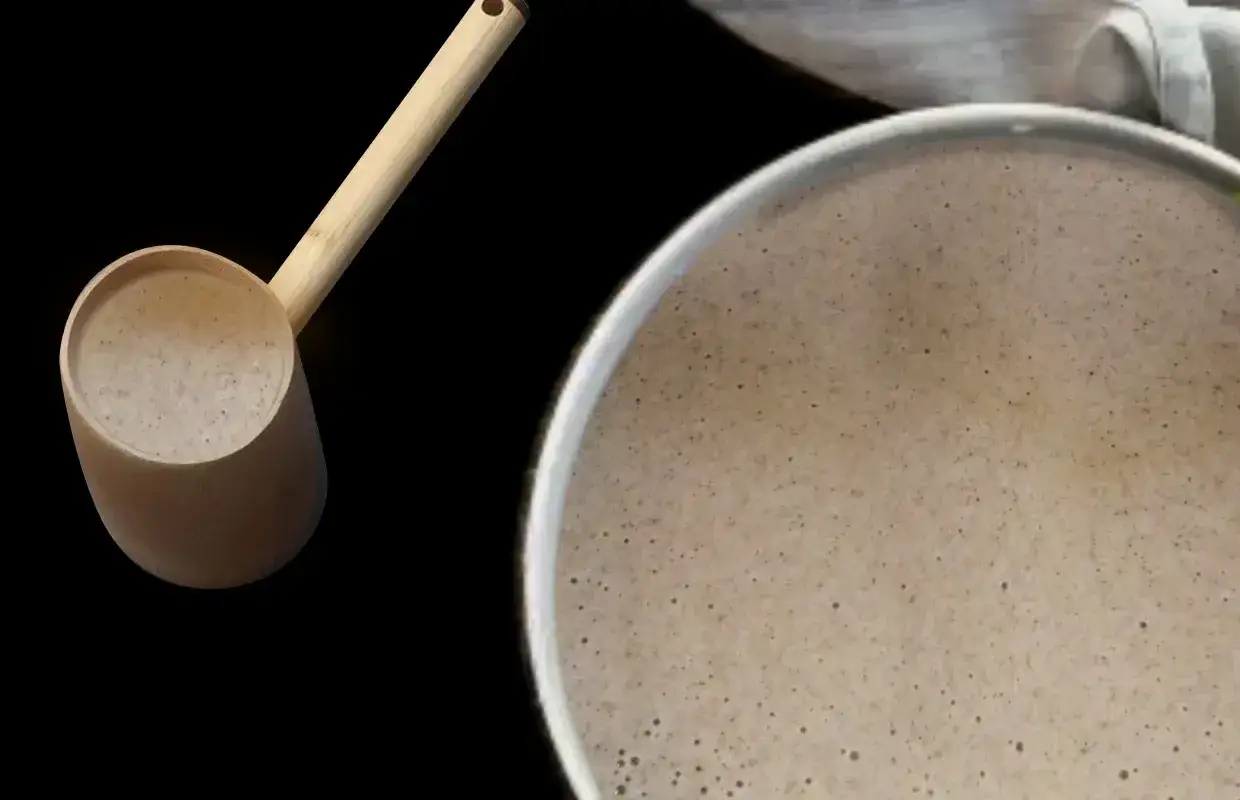 Une louche en bambou remplit de pâte à crêpes, prête pour la cuisson. La pâte repose, signe d'une bonne recette de crêpes.