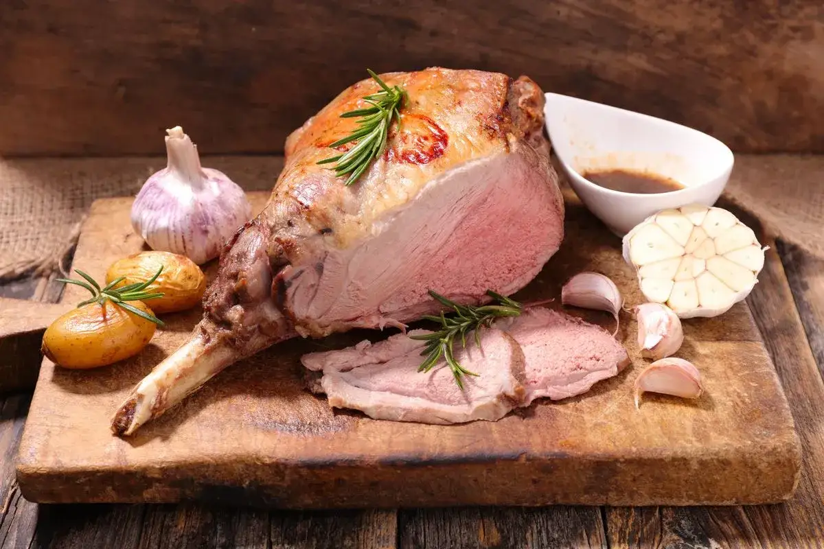 Gigot d'agneau r&ocirc;ti, parfait pour une recette d'agneau pascal. Servi avec des pommes de terre, de l'ail et du romarin.