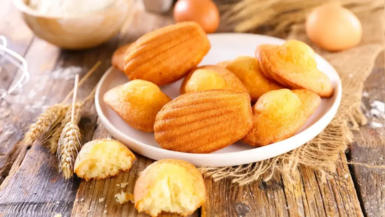 Assiette de madeleines dor&eacute;es, parfaites pour une recette madeleine moelleuse. Des &eacute;pis de bl&eacute; et des &oelig;ufs rappellent les ingr&eacute;dients frais.