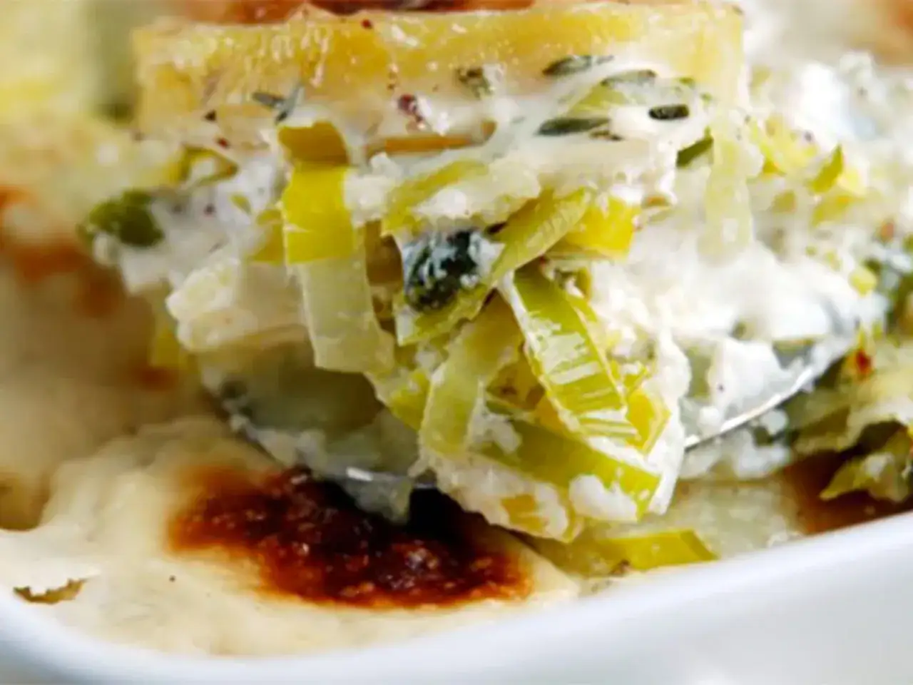Une cuill&egrave;re sert une portion g&eacute;n&eacute;reuse de gratin de poireaux cr&eacute;meux, garni de fines herbes et de pommes de terre dor&eacute;es.