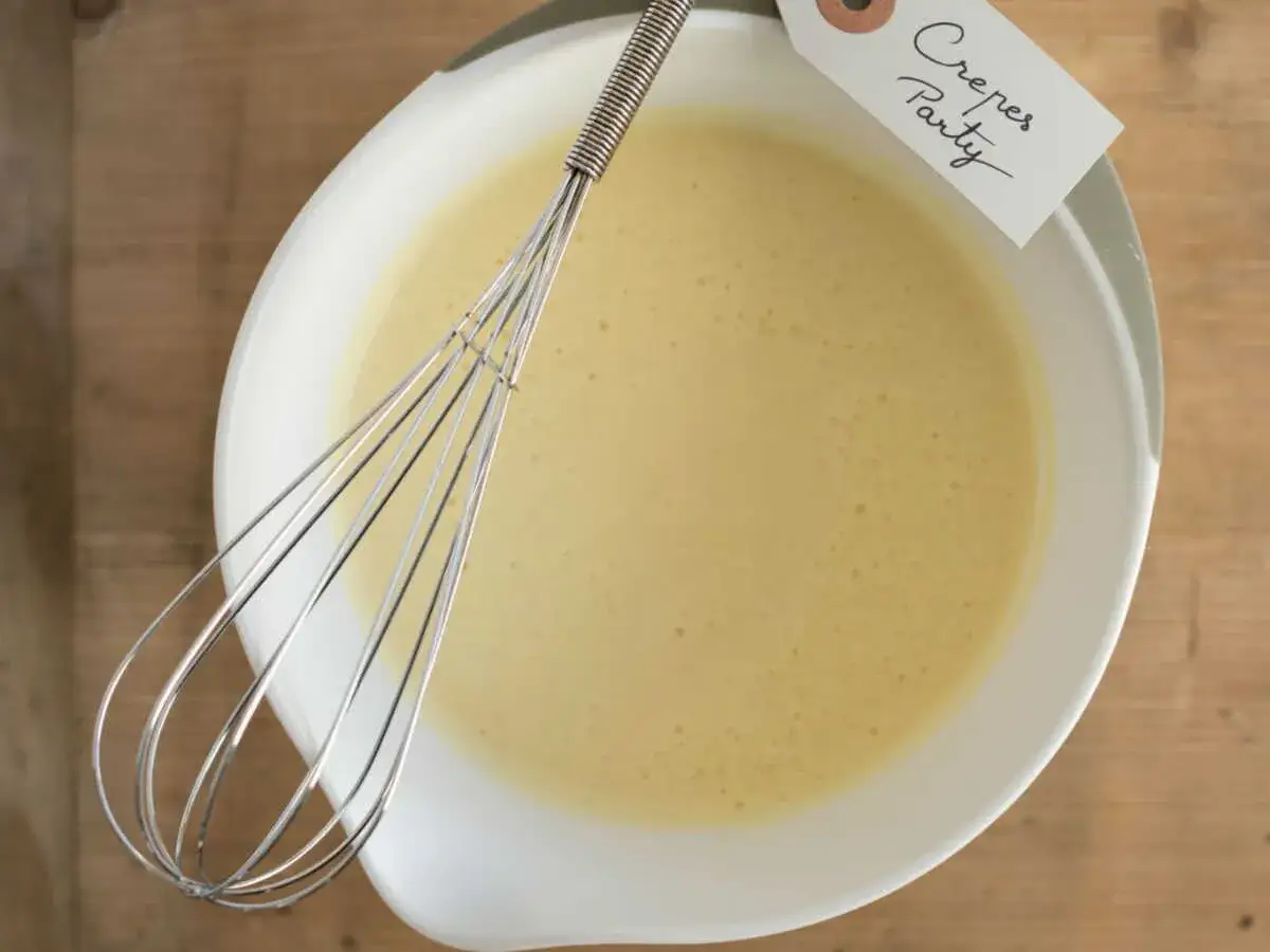 Un fouet repose dans un bol de pâte à crêpe salée au beurre, prête pour une