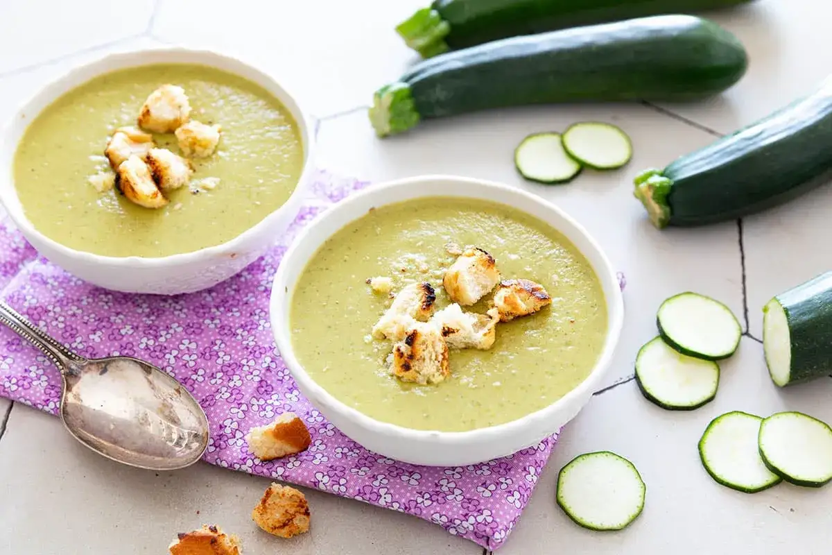 Deux bols de soupe courgette cr&eacute;meuse, garnie de cro&ucirc;tons grill&eacute;s, avec des courgettes fra&icirc;ches et des rondelles sur la table.