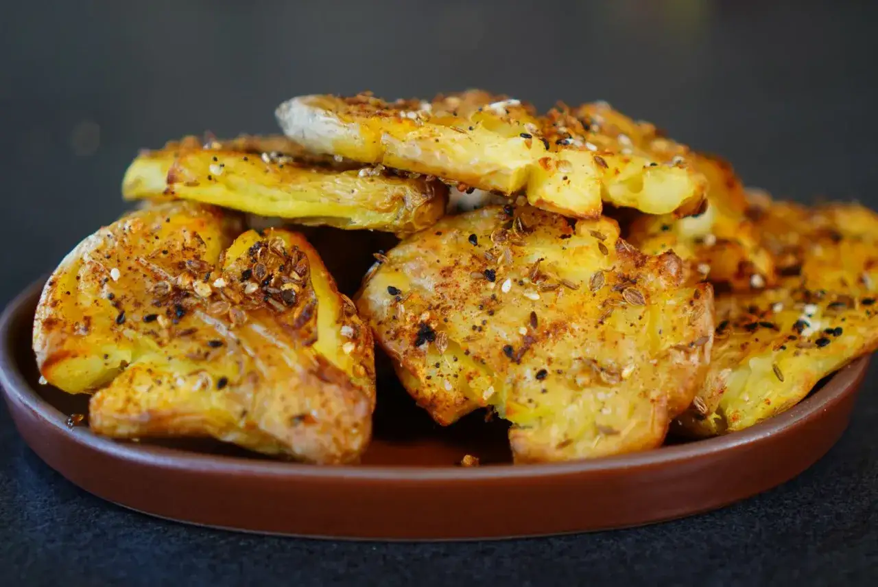 Galettes de pomme de terre croustillantes, assaisonnées d'épices et de graines, servies sur une assiette marron.