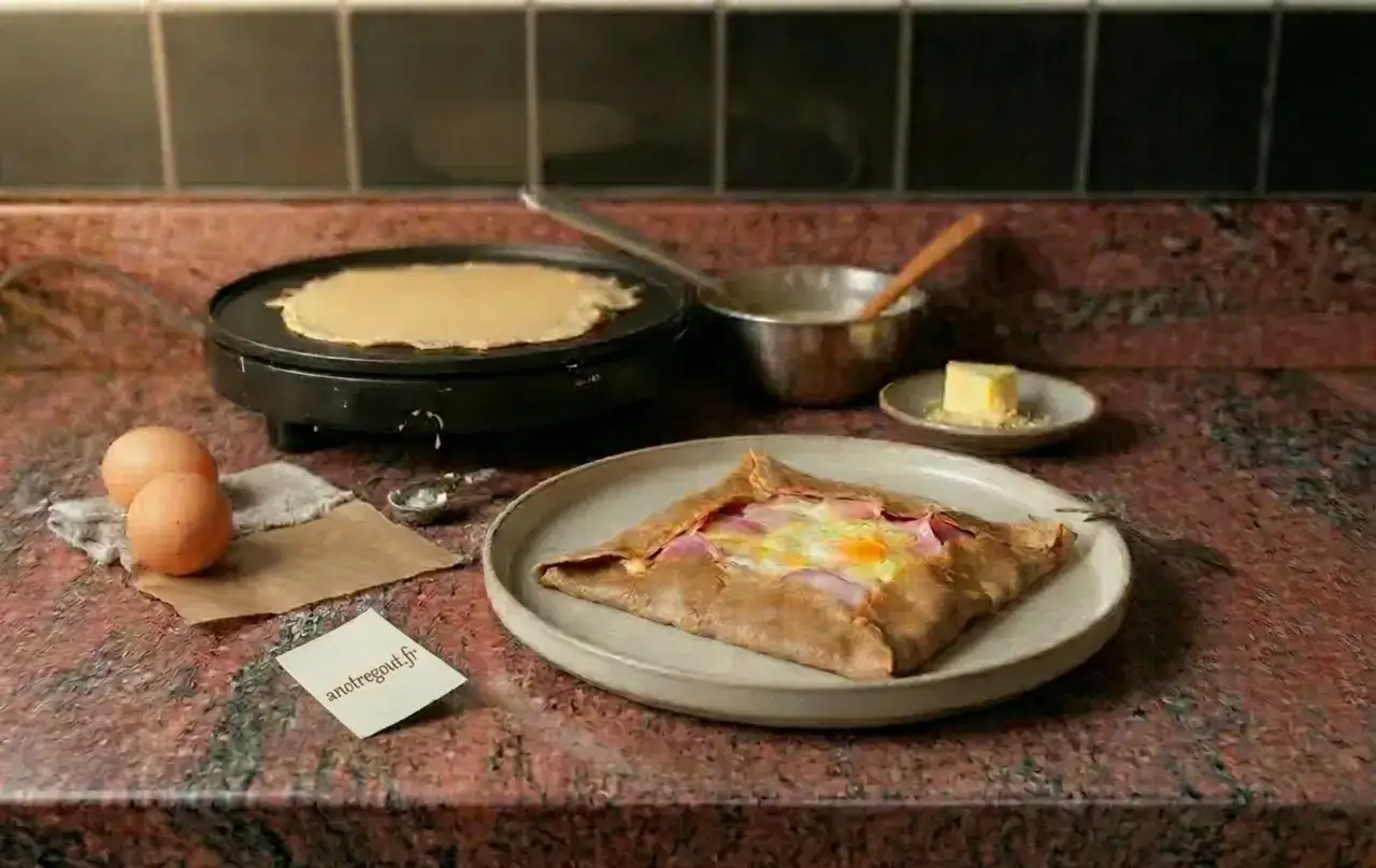 Préparation d'une galette de sarrasin pour 4 personnes : une crêpe cuit sur une crêpière, des œufs, du jambon et du fromage dans une galette garnie.