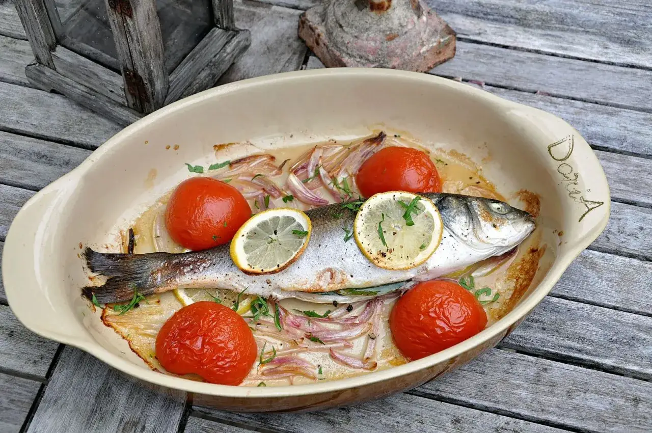 Un bar entier, pr&ecirc;t pour la cuisson au four, est pr&eacute;sent&eacute; dans un plat avec des tomates, des oignons et des rondelles de citron.