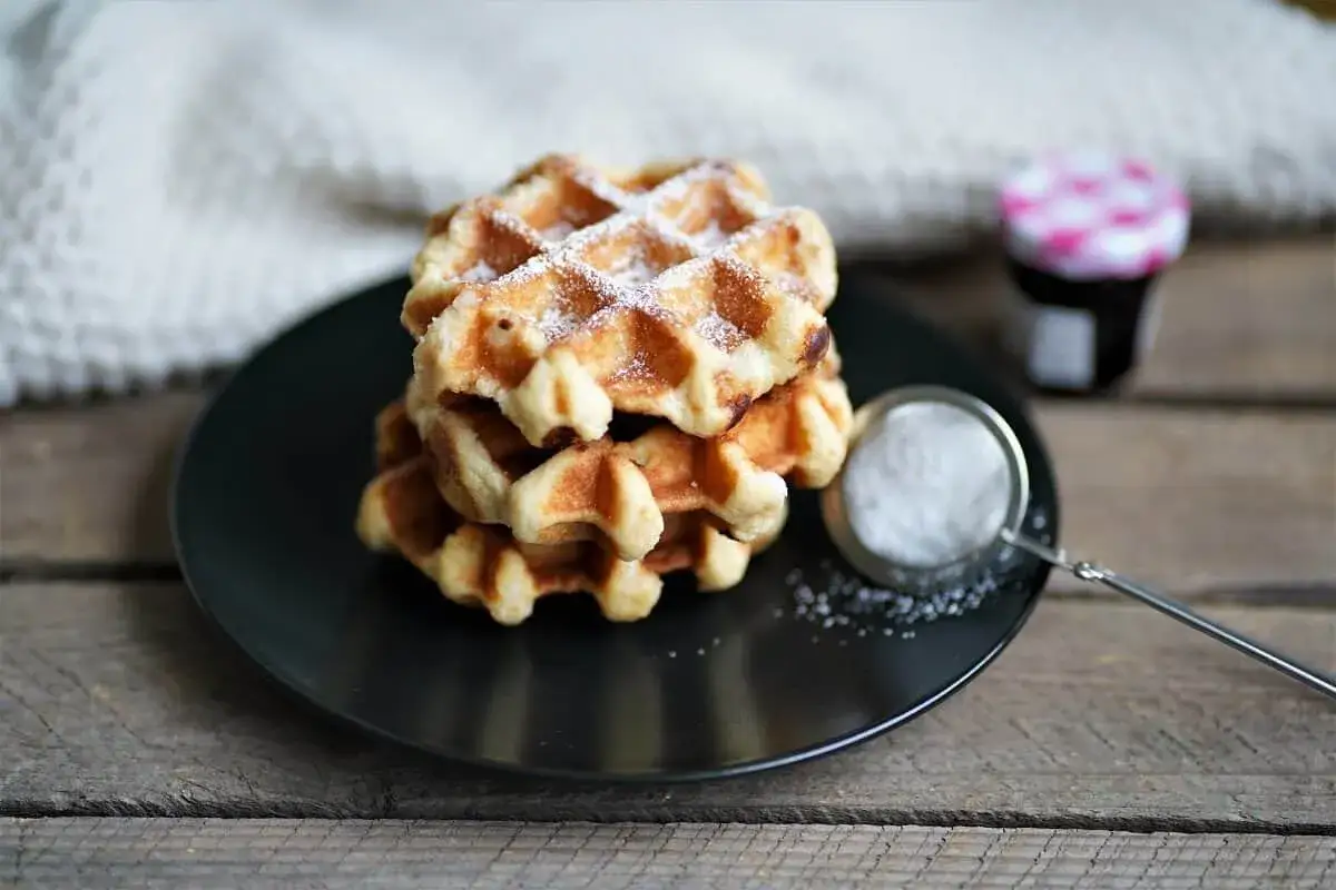 Pile de gaufres traditionnelles saupoudrées de sucre glace, prêtes à être dégustées. Une recette de gaufre traditionnelle à partager.