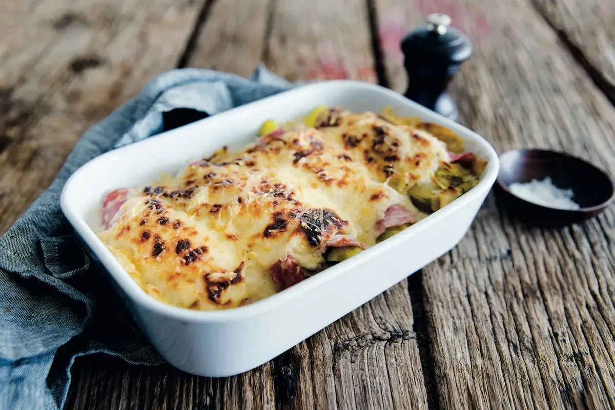 Un plat gratiné d'endives au jambon, recouvert de fromage doré, sur une table en bois rustique.