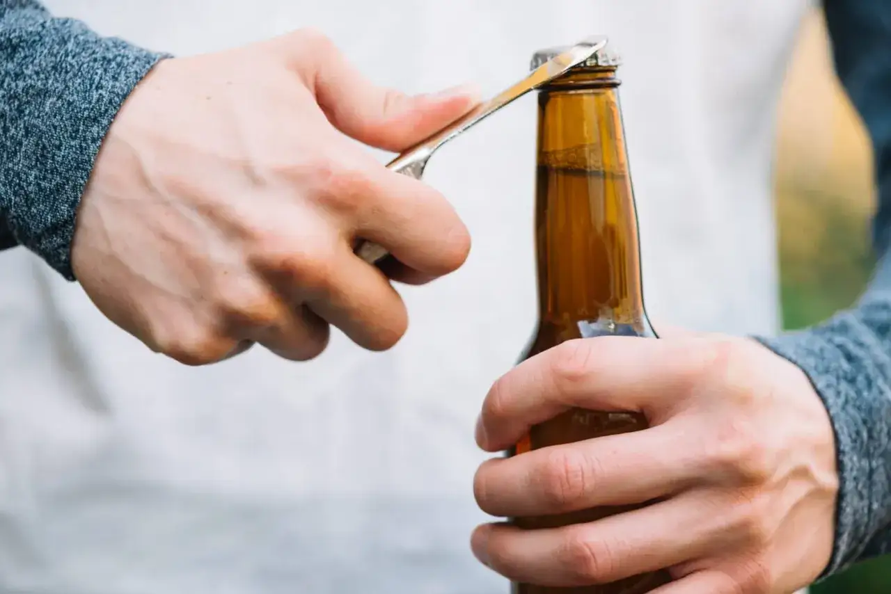 Main tenant, une bouteille de bi&egrave;re ambr&eacute;e, utilise un objet pour ouvrir le goulot. Une astuce pour ouvrir une bouteille sans tire bouchon.