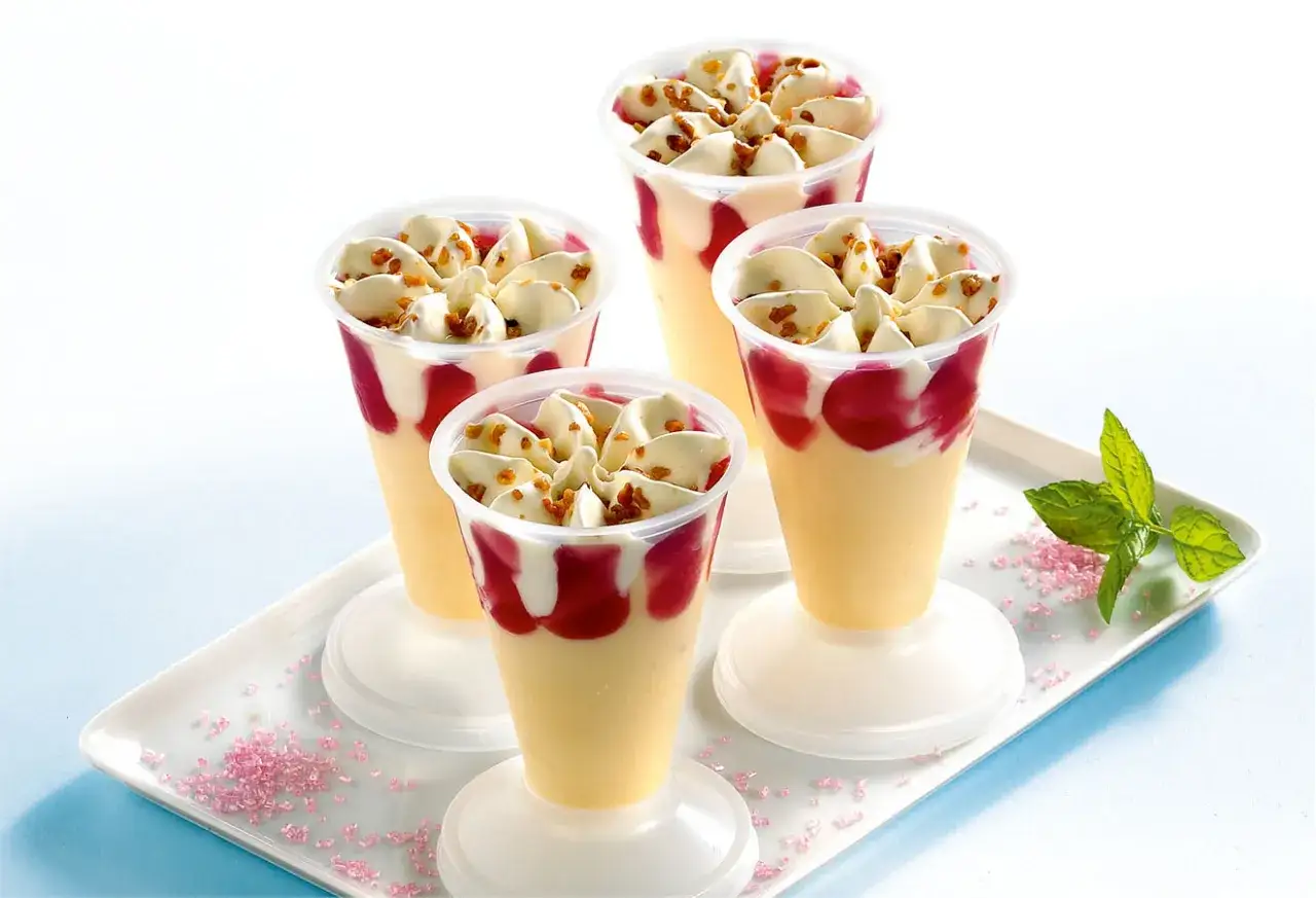Quatre coupes de glace p&ecirc;che melba, garnies de fruits rouges et de croquant.