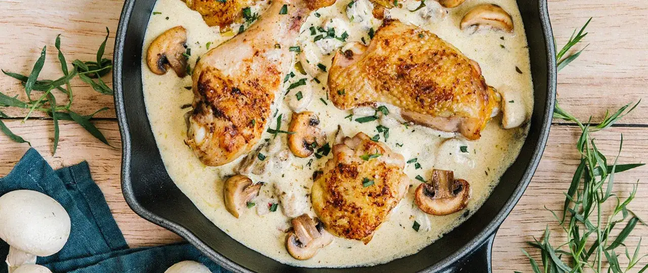 Un plat de poulet &agrave; la cr&egrave;me onctueuse, parsem&eacute; de champignons et d'herbes fra&icirc;ches, servi dans une po&ecirc;le en fonte.