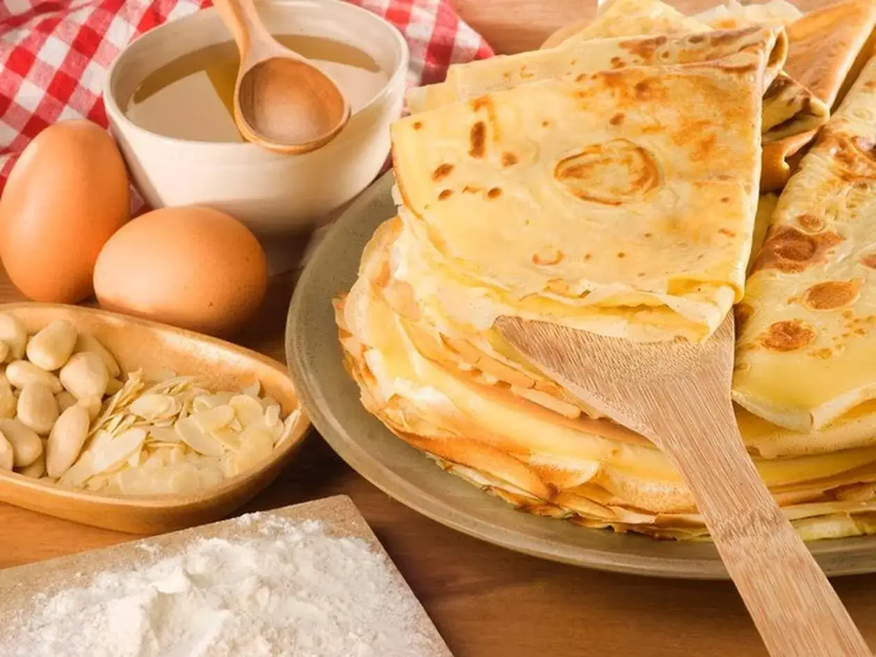 Une pile de crêpes dorées, des œufs, des amandes et de la farine, ingrédients pour la meilleure recette de pâte à crêpes.