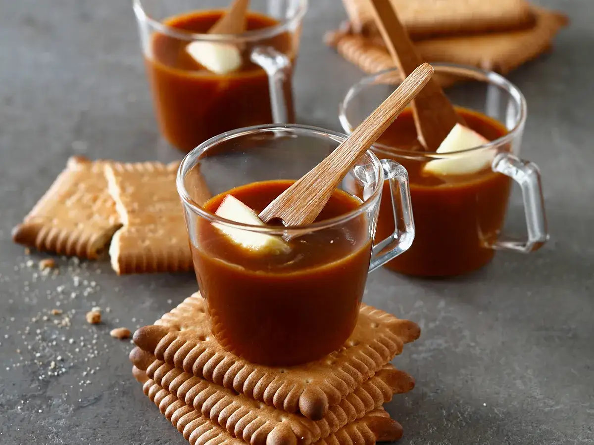 Trois tasses de caramel liquide avec des morceaux de pomme, accompagn&eacute;es de biscuits. Un d&eacute;lice r&eacute;confortant.