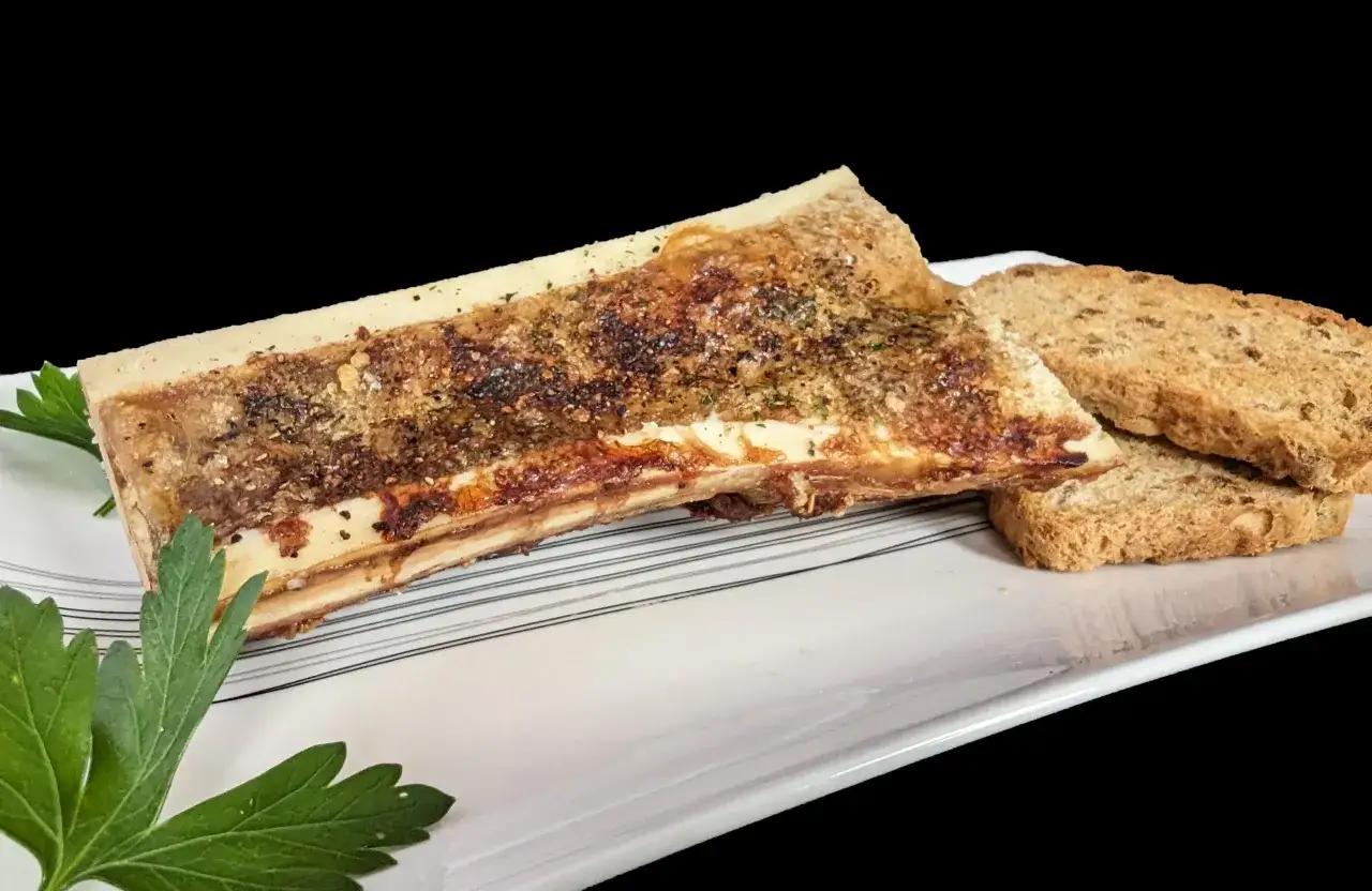 Un os &agrave; moelle r&ocirc;ti, assaisonn&eacute; et garni d'herbes, servi avec des toasts croustillants sur une assiette blanche.