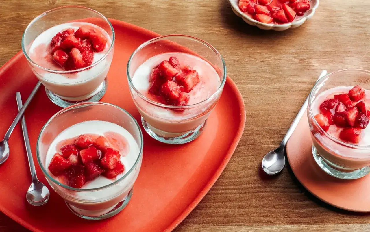 Quatre panna cotta fraise crémeuses dans des verres, garnies de fraises fraîches coupées. Un délice estival.