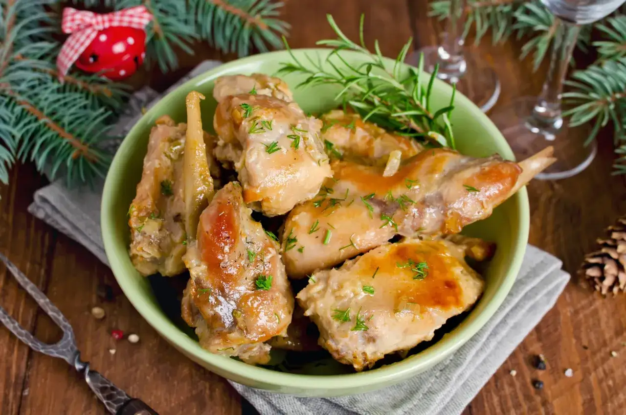 D&eacute;licieux lapin au four, servi dans un bol vert avec des herbes fra&icirc;ches. Une touche festive avec des branches de sapin et une clochette rouge.