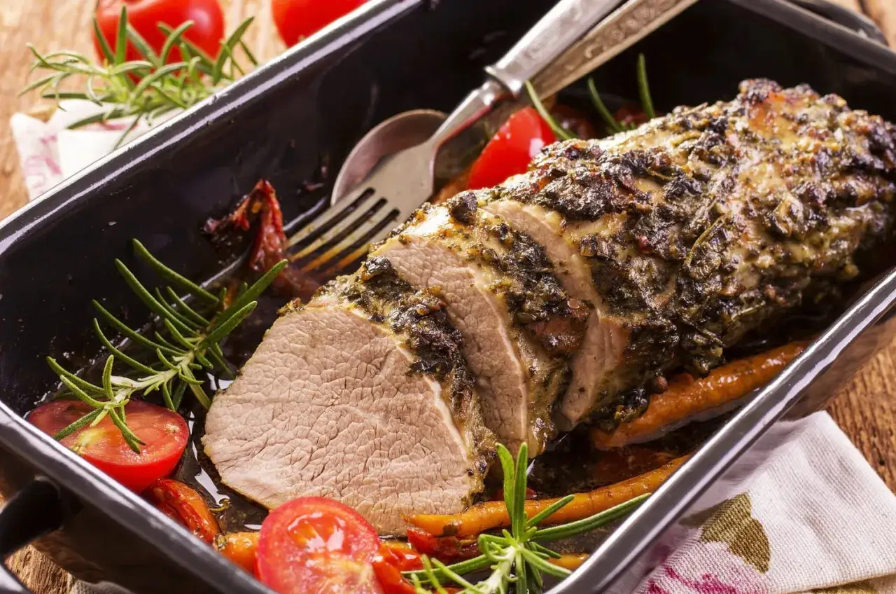 Un d&eacute;licieux roti de veau aux herbes, tranch&eacute; et servi dans un plat avec des tomates cerises et du romarin.