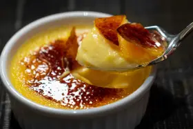 Une cuillère prélève un morceau de crème brûlée, révélant sa texture onctueuse sous une croûte de caramel craquante.