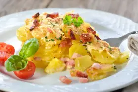 Un délicieux gratin de pommes de terre et lardons, doré au four, servi avec des tomates cerises et du basilic. Un plat réconfortant et savoureux.