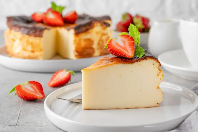 Tranche de gâteau au fromage brûlé, garnie de fraises et de menthe. Un dessert facile qui impressionne, parfait pour toute occasion.