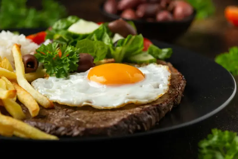 Un plat de steak a cheval savoureux avec un œuf au plat, des frites dorées, du riz blanc et une salade fraîche.