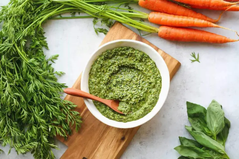 Un bol de pesto de fanes de carottes, avec des carottes fraîches et du basilic à côté.