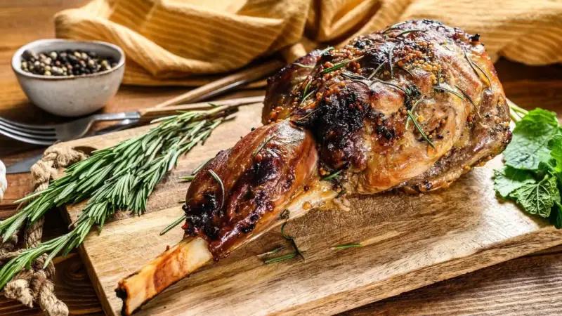 Gigot d'agneau rôti, doré et savoureux, garni de romarin et de moutarde, prêt à être dégusté.